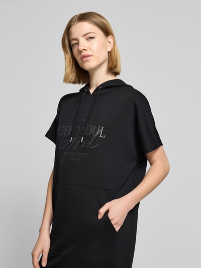 Frauenmodel trägt Sweatkleid mit Kapuze von Soyaconcept in Schwarz, Modal-Mix, Gerader-Schnitt, Label-Print, Midikleid, Nahaufnahme Oberkörper.