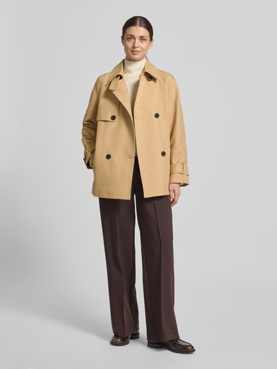Frauenmodel trägt Trenchcoat mit Ärmelriegeln von Stefanel in Beige, zweireihig, Baumwolle, Regular Fit, Eingrifftaschen, Ganzkörperansicht von vorne.