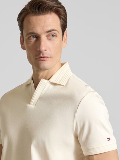 Männermodel trägt Regular Fit Poloshirt aus reiner Baumwolle von Tommy Hilfiger in Creme, unifarben, Logo-Detail, Nahaufnahme Oberkörper.