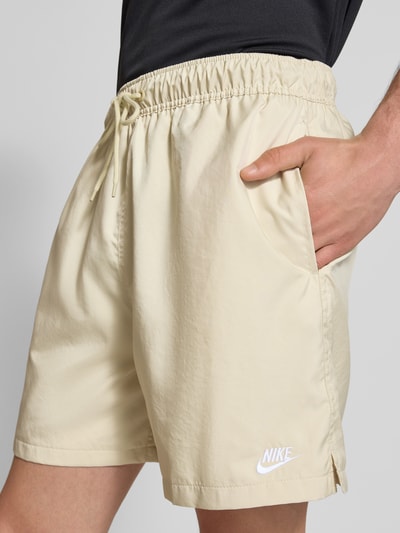 Männermodel trägt Shorts mit Label-Stitching und elastischem Bund von Nike in Beige, Regular-Fit, Tunnelzug, Nahaufnahme Oberschenkel. Kontext: Herren Shorts, Regular Fit, Label-Stitching, elastischer Bund, Tunnelzug, Bundweite Größe M 41 cm, Innenbeinlänge 14 cm.