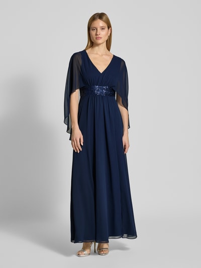 Modelka nosi 'Abendkleid mit Taillenband und Pailletten' od SWING, szyfon, linia A, długa sukienka, dekolt w serek, tasiemka w talii z cekinami, długość tyłu w rozmiarze 36: 149 cm, szerokość klatki piersiowej w rozmiarze 36: 35 cm, widok całej sylwetki z przodu.