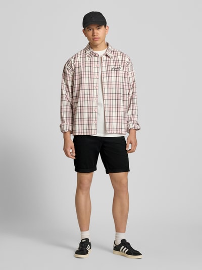 Männermodel trägt schwarze Shorts mit Gürtel Modell 'MIKE' von Redefined Rebel, kombiniert mit karierter Hemdjacke, Ganzkörperansicht von vorne. Herren Shorts mit Regular Fit, Eingrifftaschen, Gesäßtaschen, Bundweite 43 cm, Innenbeinlänge 21 cm.