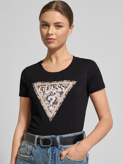 Frauenmodel trägt Slim Fit T-Shirt mit Ziersteinbesatz von Guess aus elastischem Baumwoll-Mix, Logo-Detail, Rundhalsausschnitt, Nahaufnahme Oberkörper.