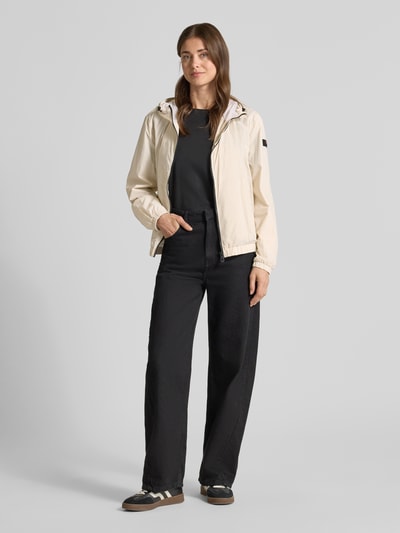 Frauenmodel trägt Regular Fit Jacke mit Kapuze Modell 'Nigle' von Peuterey in Beige mit Eingrifftaschen, elastische Abschlüsse, Zweiwege-Reißverschluss, Rückenlänge 60 cm, Schulterbreite 47 cm, Brustweite 57 cm, Ärmellänge 61 cm, Ganzkörperansicht von vorne.