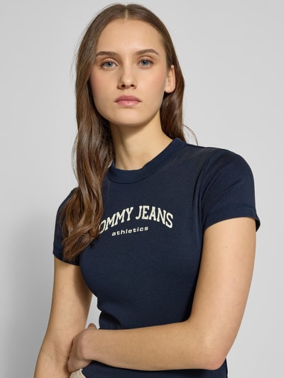 Vrouwenmodel draagt unifarben donkerblauw Slim Fit T-Shirt aus Baumwoll-Mix Modell 'SLIM VARSITY' van Tommy Jeans met labelprint, ronde hals en korte mouwen, Nahaufnahme bovenlichaam.