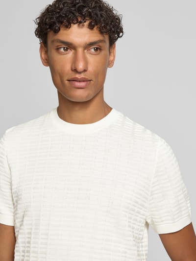 Männermodel trägt T-Shirt mit Label-Detail Modell 'Theor' von JOOP! Collection in Offwhite, feine Struktur, Rundhalsausschnitt, Nahaufnahme Oberkörper.
