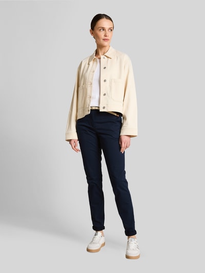 Modelka nosi Slim Fit Chino aus Baumwoll-Mix von Tom Tailor, efekt: jednolity kolor, krój slim fit, szlufki na pasek, szwy w kontrastowym kolorze, zapięcie na guzik i zamek błyskawiczny, pasek, zakończenie nogawek: brzeg, wpuszczane kieszenie, kieszenie z tyłu, mieszanka bawełny, Ganzkörperansicht von vorne.