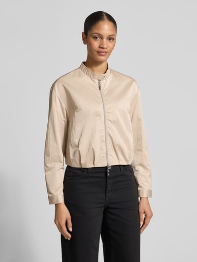 Vrouwenmodel draagt Cropped Jacke met Zweiwege-Reißverschluss van monari in beige, met opstaande kraag en knoopsluiting, geheel vooraanzicht. Ruglengte 49 cm, schouderbreedte 50 cm, borstwijdte 44 cm, mouwlengte 56 cm.