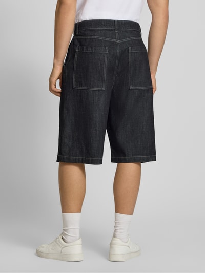 Męski model nosi Extra Baggy Fit bermudy model LLOYD od Jack & Jones z czarnej bawełny, wpuszczane kieszenie, szerokość w rozmiarze M 41 cm, długość wewnętrzna nogawki 30 cm, widok całej sylwetki od tyłu.