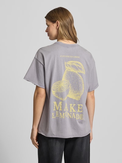 Vrouwenmodel draagt oversized T-shirt uit biologisch katoen model 'KINNA LIFE' van Only met gemêleerde look, gele tekstapplicatie, ronde hals, korte mouw, open zoom met rolzoom, detailopname rugaanzicht