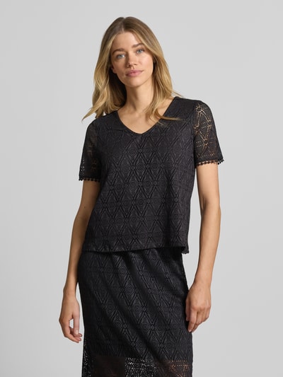 Frauenmodel trägt Regular Fit T-Shirt in Heckel-Optik Modell 'MAYA' von Vero Moda, schwarz, Allover-Muster, V-Ausschnitt, kurzarm, Ganzkörperansicht von vorne.