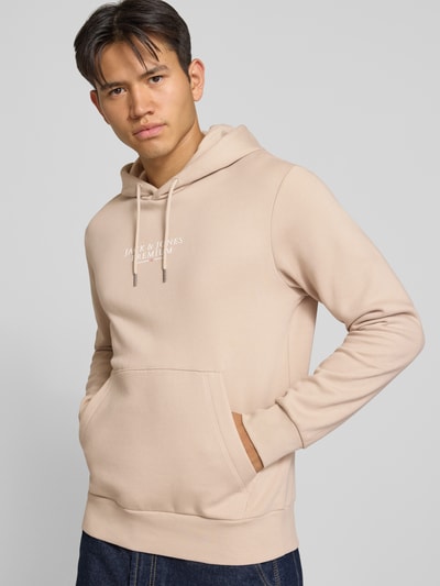 Männermodel trägt beigen Hoodie mit Label-Print Modell 'JPRBLUARCHIE' von JACK & JONES, lockerer Schnitt, Baumwoll-Mix, Ganzkörperansicht von vorne.