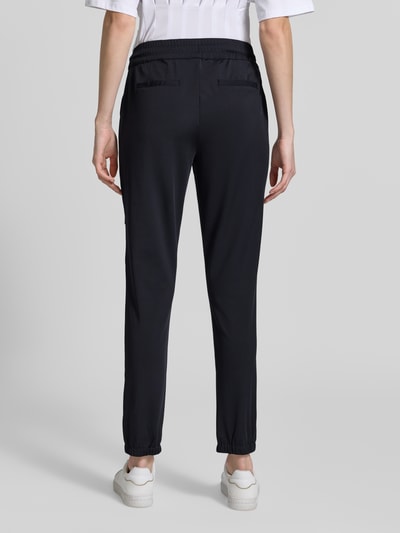 Frauenmodel trägt Jogpants mit elastischem Bund Modell 'Jill' von monari, Material-Mix mit Stretch-Anteil, Regular-Fit, dunkle Farbe, Ganzkörperansicht Rückansicht.