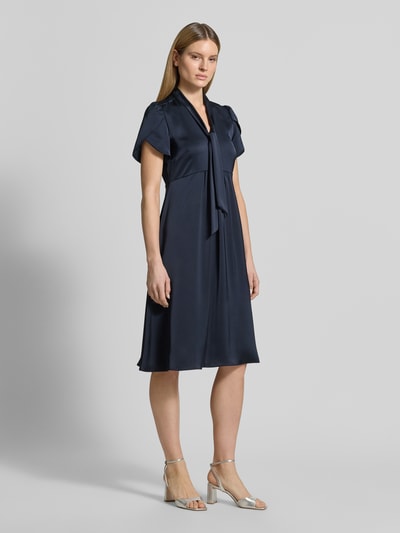 Frauenmodel trägt Midikleid mit V-Ausschnitt und Schluppe von Christian Berg Woman Selection aus dunkelblauem Satin mit A-Linie, Schmetterlingsärmel, seitlichem Nahtreißverschluss, Rückenlänge bei Größe 36: 111 cm, Brustweite bei Größe 36: 46 cm, Ganzkörperansicht von vorne.