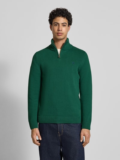 Männermodel trägt Slim Fit Pullover in Strick-Optik von Superdry in Grün mit Stehkragen, Reißverschluss, Logo-Stitching, Ganzkörperansicht von vorne. Rückenlänge bei Größe M 70 cm, Ärmellänge 65 cm.