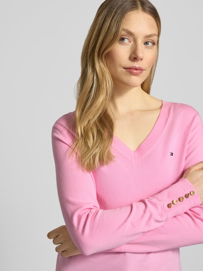 Vrouwenmodel draagt Regular Fit gebreide pullover uit puur katoen van Tommy Hilfiger, effen kleuren, gestikt logo, sierknopen, lange mouw, V-hals, geribde boorden, gestreept motief, soft knitwear, all-over motief, detailopname bovenlichaam.