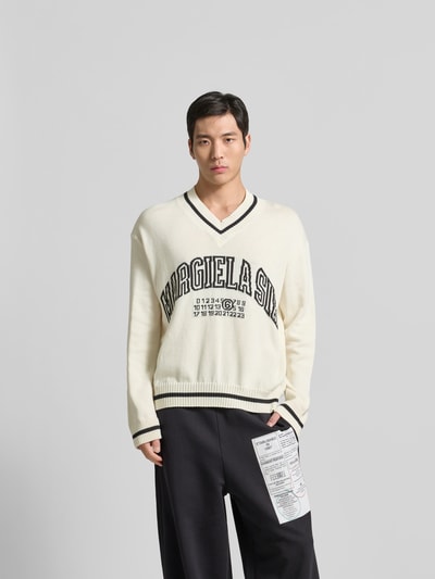 Männermodel trägt Pullover in Strick-Optik von MM6 Maison Margiela in Creme mit Logo-Print, lockerer Passform, Nahaufnahme Oberkörper.