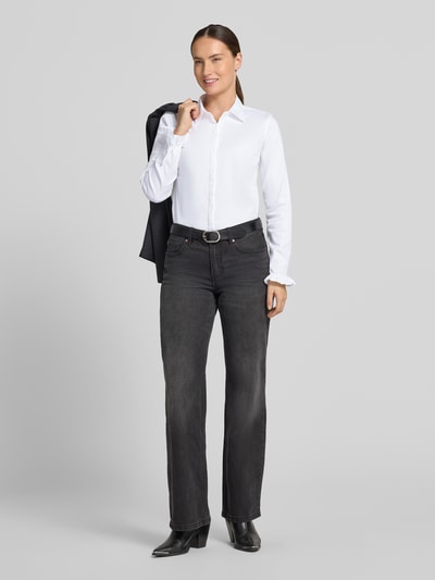Kobiece modelka nosi bluzkę koszulową z mieszanki bawełny Model 'Mattie' od MOS MOSH, krój slim fit, białe, z listwą guzikową, długie rękawy, falbany przy zakończeniach rękawów, kołnierzyk koszulowy, zaokrąglony dół, długość tyłu w rozmiarze S: 70 cm, długość rękawów w rozmiarze S: 62 cm, widok całej sylwetki z przodu.