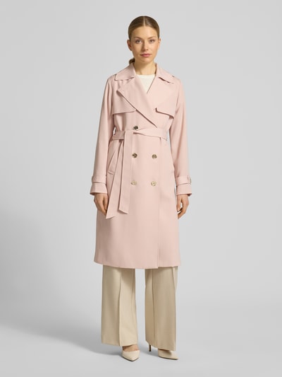 Vrouwenmodel draagt Zweireihiger Trenchcoat mit Bindegürtel van MICHAEL Michael Kors in lichtroze, double-breasted, reverskraag, regular fit, met riem, beige broek en pumps, lichte achtergrond. Volledig lichaamsaanzicht van voren.