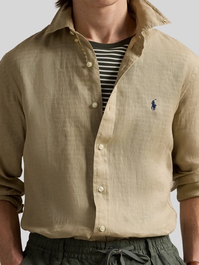 Mężczyzna nosi Slim Fit Freizeithemd aus reinem Leinen von Polo Ralph Lauren, jednolity kolor, krój slim fit, kołnierzyk typu button down, listwa guzikowa na całej długości, wyhaftowane logo, długi rękaw z mankietami sportowymi, materiał: czysty len. Zbliżenie na górną część ciała.