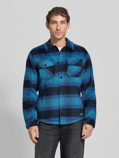 Männermodel trägt Regular Fit Hemdjacke mit Brusttaschen von Scotch & Soda in Blau-Schwarz-Karomuster, Ganzkörperansicht von vorne. Mix mit Woll-Anteil, Allover-Look, Kentkragen, Knopfleiste, Rückenlänge bei Größe M: 72 cm.