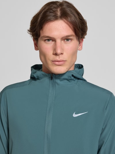 Männermodel trägt Trainingsjacke mit Logo-Print und Stehkragen von NIKE TRAINING, Reißverschluss, seitliche Eingrifftaschen, elastische Ärmelabschlüsse, Nahaufnahme Oberkörper.