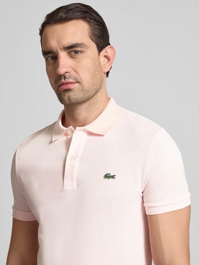 Mężczyzna-model nosi Slim Fit Poloshirt aus reiner Baumwolle od Lacoste, efekt: jednolity kolor, wyhaftowane logo, kołnierzyk polo, krótki rękaw, prążkowane zakończenie rękawów, wykończenie z rozcięciami po bokach, pika, bawełna; zbliżenie na górną część ciała z przodu.
