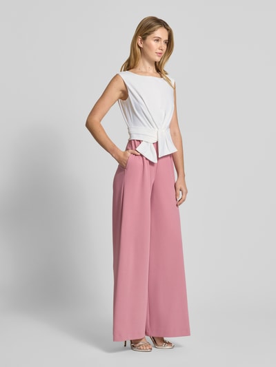 Kobiece model prezentuje Kombinezon mit Knotendetail von Vera Mont, mieszanka materiałów z dodatkiem streczu, krój regular fit, okrągły dekolt, różowe i białe kolory, całkowita długość 150 cm, długość wewnętrzna nogawki 83 cm, długość tyłu 39 cm w rozmiarze 36, szerokość klatki piersiowej 30 cm w rozmiarze 36, widok całej sylwetki z przodu.