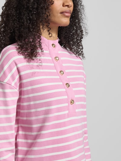 Frauenmodel trägt Ringel Polo Shirt mit Schmuckknopf von Christian Berg Woman in Rosa-Weiß mit geripptem Stehkragen, Lockere-Schnitt, kurze Knopfleiste, Rückenlänge 52 cm bei Größe S, Nahaufnahme Oberkörper.