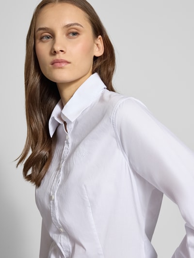 Frauenmodel trägt Slim Fit Bluse mit Knopfleiste von Guess Jeans, weiße Baumwolle, Hemdblusenkragen, Nahaufnahme Oberkörper.