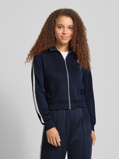 Vrouwenmodel draagt Regular Fit Trackjacke met logostitching van Review, donkerblauw, opstaande kraag, met kant, ritssluiting, steekzakken, elastische boorden. Ganzkörperansicht van voren.