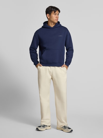 Männermodel trägt Straight Fit Sweatpants aus Baumwoll-Mix mit Label-Detail von REVIEW in Beige, elastischer Bund, Eingrifftaschen, Ganzkörperansicht von vorne.