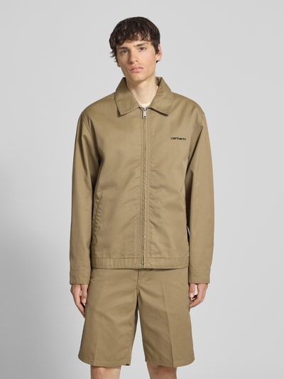Męski model nosi Jacke mit Label-Stitching und Eingrifftaschen von Carhartt Work In Progress, beż, krój regular fit, wykładany kołnierz, zamek błyskawiczny, wyhaftowane logo, wpuszczane kieszenie, długość tyłu w rozmiarze M: 68 cm, szerokość ramion w rozmiarze M: 59 cm, szerokość klatki piersiowej w rozmiarze M: 60 cm, długość rękawów w rozmiarze M: 20 cm, gładka tekstura, całkowity widok z przodu