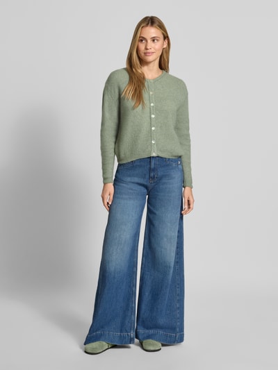 Frauenmodel trägt Relaxed Fit Strickjacke aus Woll-Mix mit Leinen-Anteil von American Vintage, hellgrün, gerippte Bündchen, Ganzkörperansicht von vorne.