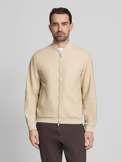 Męski model nosi Jacke aus Baumwoll-Leinen-Mix mit Zweiwege-Reißverschluss von Jack & Jones Premium, krój regular fit, stójka, mieszanka bawełny i lnu, kolory jasny beż i brąz, tekstura gładka, długość tyłu w rozmiarze M 68 cm, szerokość ramion w rozmiarze M 45 cm, szerokość klatki piersiowej w rozmiarze M 54 cm, długość rękawów w rozmiarze M 66 cm, całkowity widok z przodu