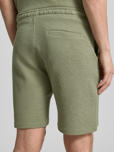 Männermodel trägt Sweatshorts mit elastischem Bund von MCNEAL in grünem Elastischer-Material-Mix, Strukturmuster, Rückansicht Detailaufnahme. Herren Shorts mit Gerader Passform, Tunnelzug, Eingriff- und Gesäßtaschen, Bundweite 43 cm, Innenbeinlänge 21 cm bei Größe M.