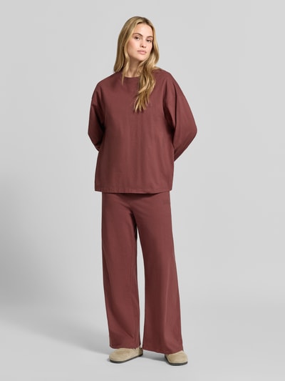 Vrouwenmodel draagt Relaxed Fit Langarmshirt uit katoen van American Vintage, trendy bordeauxrood met ribgebreide bies, ronde hals, schouderpartij met verlaagde schoudernaden, met lange mouwen, ruglengte maat XS/S 64 cm, geheel lengtevooraanzicht.