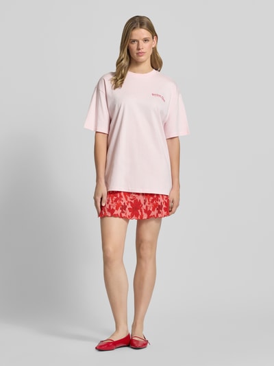 Vrouwenmodel draagt Ausgestellter Mini-Rock met all-over motief model 'FLORA' van Pieces, rood met roze accenten, dames mini-rok, ganzijnaanzicht van voren.