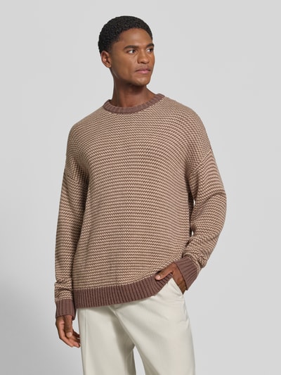 Männermodel trägt Relaxed Fit Strickpullover mit Streifen-Muster Modell 'NEELIO' von DRYKORN, beige-braune Töne, Nahaufnahme Oberkörper. Material-Mix mit Woll-Anteil, elastische Abschlüsse, Rückenlänge 70 cm, Ärmellänge 56 cm.