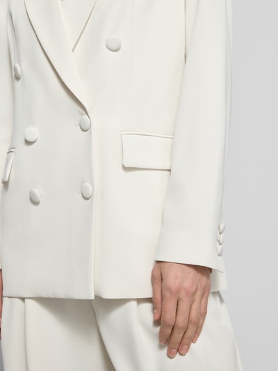 Frauenmodel trägt Regular Fit Blazer mit Pattentaschen von Christian Berg Cocktail, Material-Mix mit Stretch-Anteil, Zweireiher, Reverskragen, cremeweiß, glatte Textur, Ganzkörperansicht von vorne.