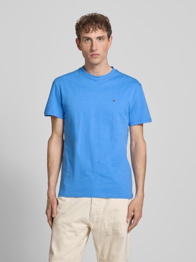 Männermodel trägt Regular Fit T-Shirt aus reiner Baumwolle von Tommy Jeans in Unifarben Blau mit Logo-Stitching, Ganzkörperansicht von vorne.
