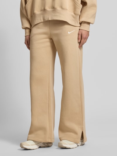 Frauenmodel trägt Wide Leg Sweatpants mit Logo Modell 'Phoenix' von Nike aus Baumwoll-Mix in Beige mit elastischem Bund und Tunnelzug, Nahaufnahme Unterkörper.