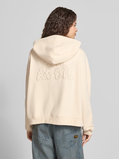 Kobiece model nosi Oversized Sweatjacke mit Zweiwege-Reißverschluss Model 'Flower' von OH APRIL z bawełny, kaptur, wyhaftowane logo, kieszeń kangurka, krój oversized, widok całej sylwetki z tyłu.