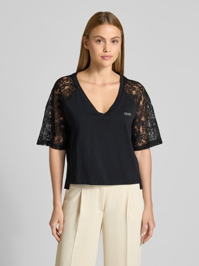 Frauenmodel trägt schwarzes T-Shirt mit Spitze und Logo-Stitching von LIU JO SPORT, V-Ausschnitt, gerade Form, Nahaufnahme Oberkörper.