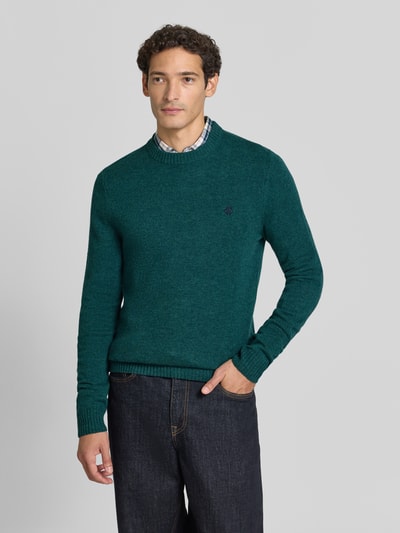 Männermodel trägt Slim Fit Strickpullover aus reiner Wolle mit Label-Stitching von MCNEAL, grüne Farbe, gerippte Abschlüsse, Ganzkörperansicht von vorne.