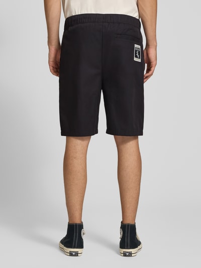 Männermodel trägt Relaxed Fit Shorts aus reiner Baumwolle von Champion in Schwarz mit elastischem Bund, Logo-Stitching, Ganzkörperansicht Rückansicht.