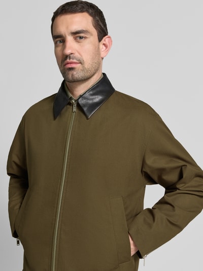 Mężczyznamodel nosi kurtka z wykładanym kołnierzem DRYKORN Jacke mit Eingrifftaschen Modell 'RIKKO', krój regular fit, wpuszczane kieszenie, zamek błyskawiczny z przodu i na rękawach, kolor oliwkowy, Długość tyłu w rozmiarze M: 69 cm, szerokość ramion w rozmiarze M: 52 cm, szerokość klatki piersiowej w rozmiarze M: 58 cm, długość rękawów w rozmiarze M: 64 cm, zbliżenie na górną część ciała, widok z przodu