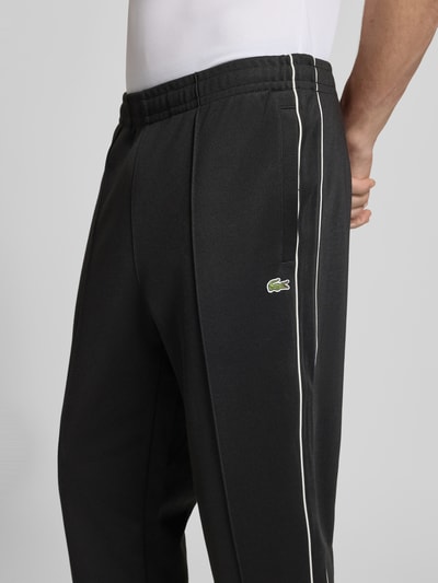 Männermodel trägt Regular Fit Sweatpants mit Baumwoll-Anteil von Lacoste, unifarben, Galonstreifen, Logo, elastischer Bund, Nahaufnahme Oberkörper.