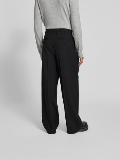 Männermodel trägt Wide Fit Stoffhose aus Woll-Mix von Filippa K in Schwarz mit Kellerfalten und Gesäßtaschen, Ganzkörperansicht Rückansicht.