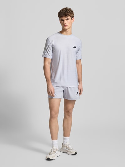 Männermodel trägt T-Shirt mit Label-Print von adidas Training in Grau, Material-Mix mit Stretch-Anteil, Regular-Fit, Ganzkörperansicht von vorne.